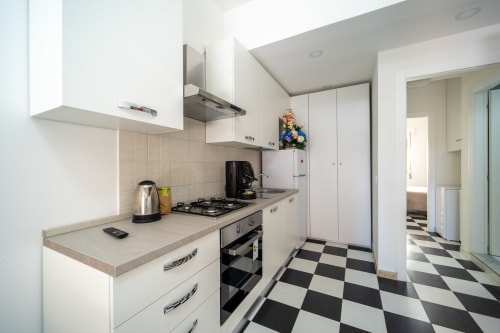 Cucina bianca moderna con fornello a gas, elettrodomestici integrati e pavimento a scacchiera bianco-nero a Marina di Strongoli