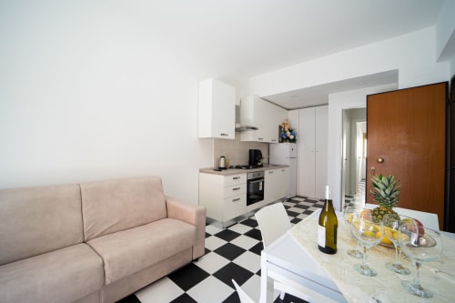Moderno appartamento open-plan a Marina di Strongoli con divano beige, cucina bianca, pavimento in piastrelle bianche e nere, e zona pranzo