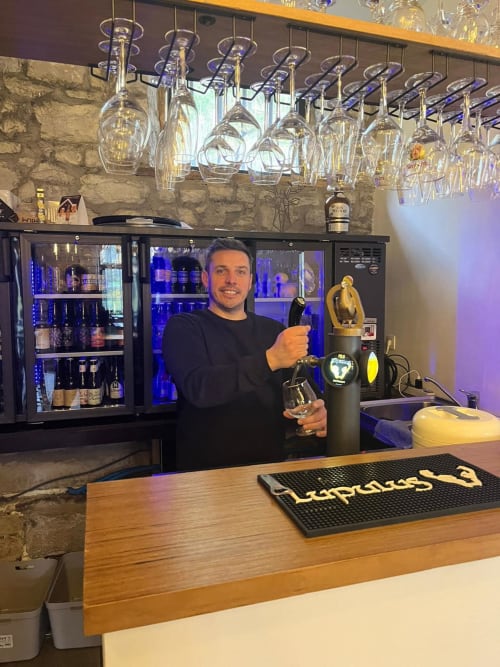 Barman du bar de l'hôtel Le Moulin Des Ramiers à Crupet versant des spiritueux premium dans des verres à vin illuminés
