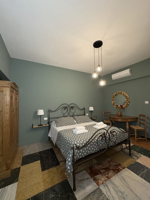 Camera elegante all'hotel Le Arche di Verona con pareti verde salvia, letto in ferro battuto, illuminazione a sospensione e pavimento in marmo