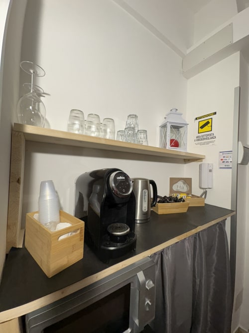 Angolo caffè nella camera dell'hotel Le Arche con macchina espresso Lavazza, bicchieri, tazze e accessori su scaffali in legno a Verona