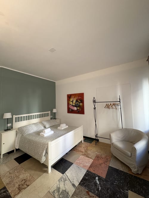 Camera dell'hotel Le Arche a Verona con letto bianco, parete verde salvia, poltrona color crema e pavimento in marmo