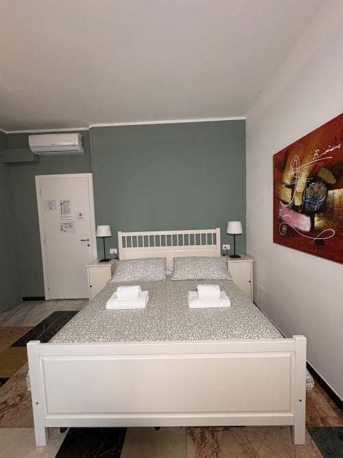 Camera moderna dell'hotel Le Arche a Verona con letto bianco, testata grigia e opera d'arte astratta rossa