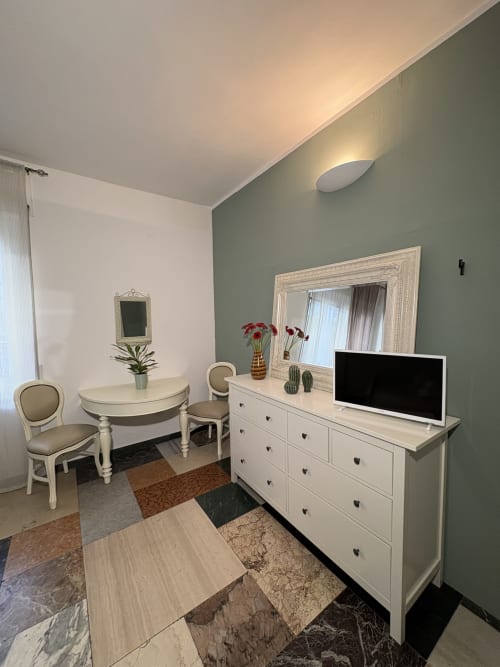 Elegante camera d'hotel Le Arche a Verona. Parete salvia, mobili bianchi, TV, specchio decorativo, stile moderno