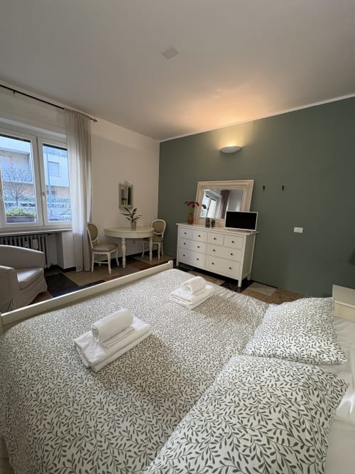 Camera spaziosa alle Le Arche Verona con letti gemelli, parete verde, comò bianco, area scrivania e grande specchio