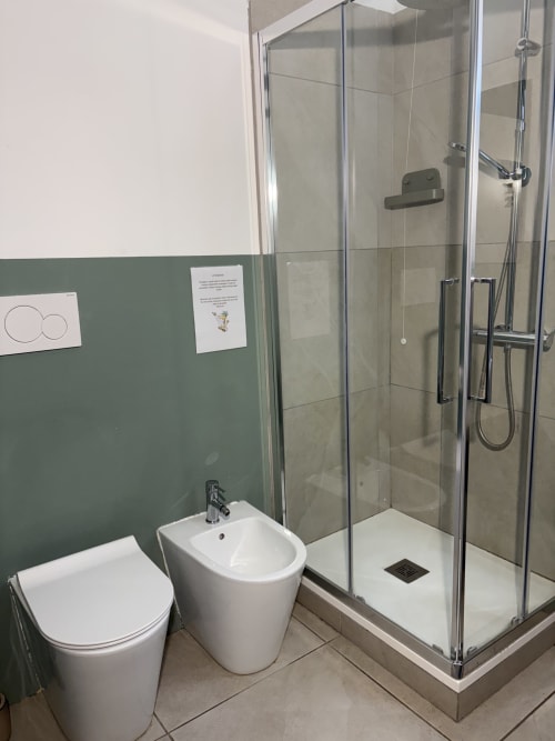 Bagno moderno dell'Hotel Le Arche a Verona con toilette bianca, bidet, box doccia e parete verde salvia