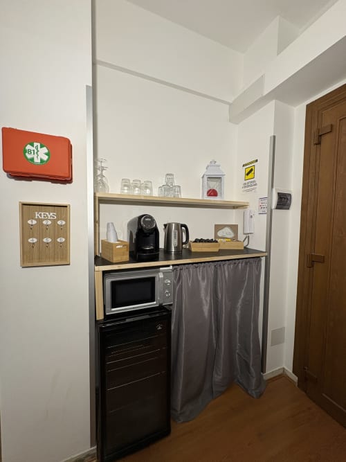 Angolo cottura compatto nella camera Tosca dell'Hotel Le Arche di Verona, con microonde, bollitore, caffettiera e scaffalature