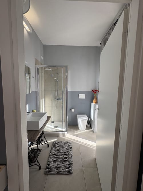 Bagno moderno dell'hotel Le Arche a Verona con doccia in vetro, lavabo, wc e pavimento in piastrelle grigie