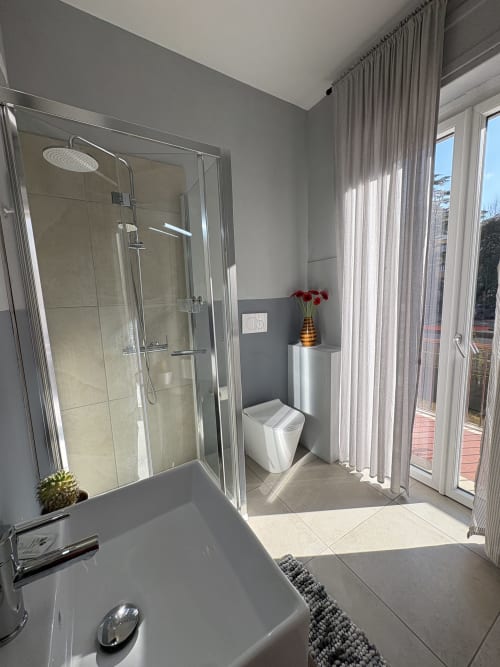 Bagno moderno dell'hotel Le Arche a Verona con doccia in vetro, wc, lavabo e accesso tramite porta in vetro al balcone