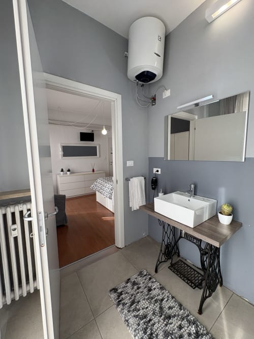 Bagno moderno dell'hotel Le Arche a Verona con lavabo design, specchio, pareti grigie e accesso alla camera da letto