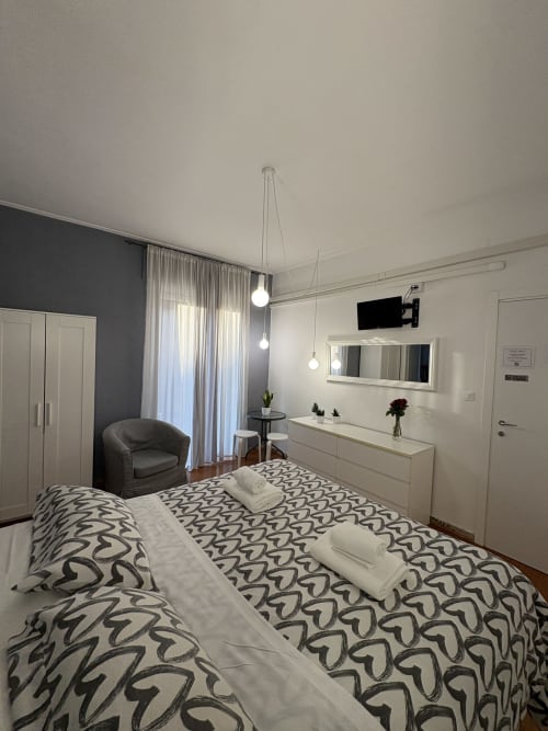 Camera moderna presso l'hotel Le Arche di Verona con letto decorato, poltrona grigia, lampade a sospensione e arredi contemporanei
