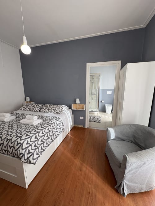 Camera moderna alle Arche Verona con letto queen, parete d'accento scura, bagno privato, poltrona e pavimenti in legno