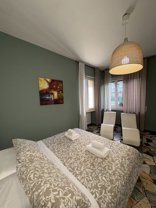 Spaziosamere dell'hotel Le Arche a Verona con pareti verde salvia, biancheria a motivi, lampada sospesa in vimini e vista sul giardino