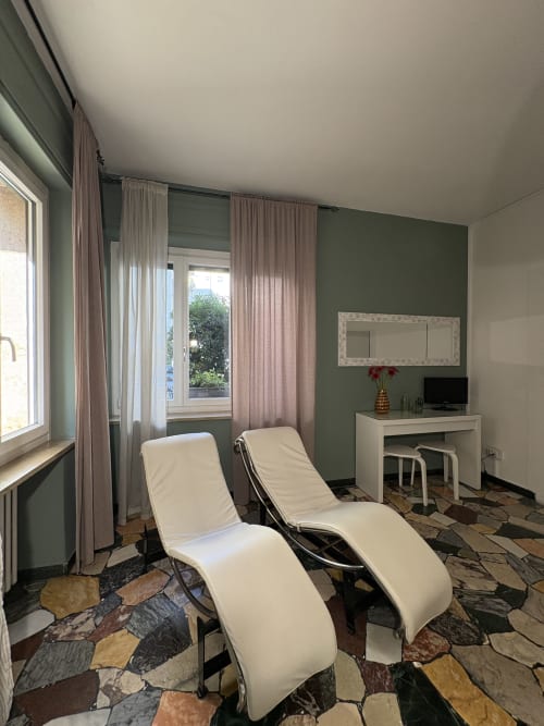 Camera moderna di Le Arche Verona con poltrone lounge, scrivania, pareti verdi e pavimento decorato