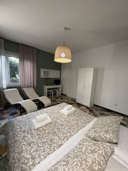 Camera moderna a Le Arche Verona con letto matrimoniale, lampada a sospensione in rattan, parete verde accento e zona relax