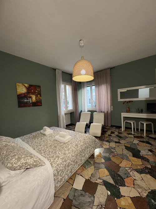 Camera moderna all'hotel Le Arche di Verona con pareti verdi, letto decorato, lampada a sospensione intrecciata e pavimento in pietra colorata
