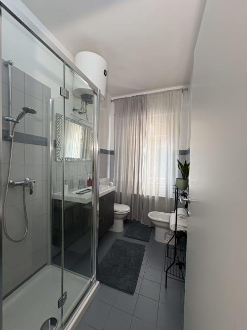 Bagno moderno nelle camere Delle Rose presso l'hotel Le Arche a Verona, con doccia in vetro, doppi lavandini e piastrelle neutre