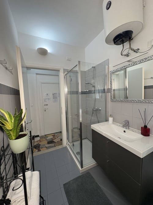 Bagno moderno dell'hotel Le Arche a Verona con doccia a filo pavimento, mobile lavabo scuro e piante decorative