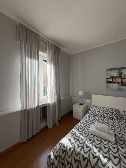 Camera moderna all'hotel Le Arche di Verona con letto a cuori, comodino bianco con lampada e tende in tulle