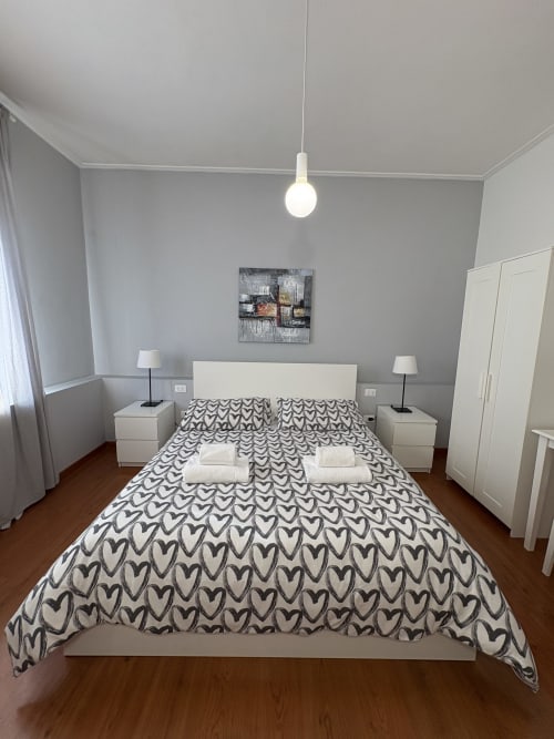 Camera moderna dell'hotel Le Arche a Verona con arredi bianchi, biancheria con motivi a cuore e luci a sospensione