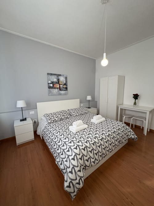 Camera moderna all'hotel Le Arche di Verona con letto matrimoniale, biancheria con motivi a cuore, arredi bianchi e pavimenti in legno