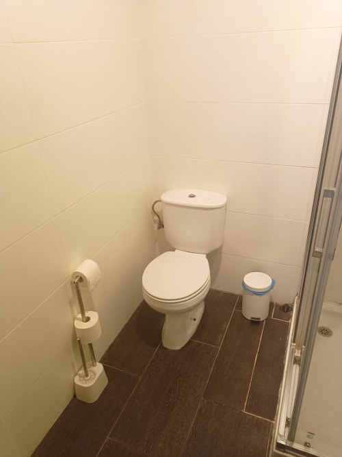 Baño limpio con inodoro blanco, bidé y piso de cerámica efecto madera oscura en departamento de Mérida