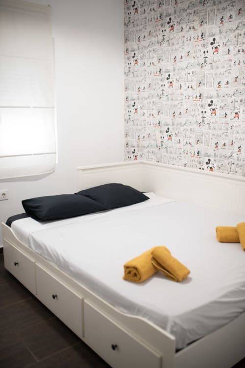 Moderna habitación en apartamento Gestyp-AT en Mérida con cama blanca, almohadas negras, toallas amarillas y papel tapiz de Mickey Mouse