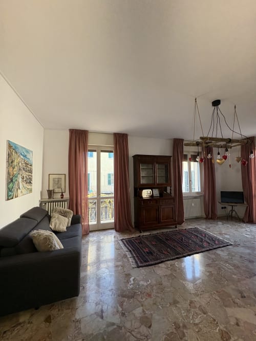 Ampio soggiorno dell'appartamento a Verona con pavimenti in marmo, divano scuro, mobili in legno e tende bordeaux
