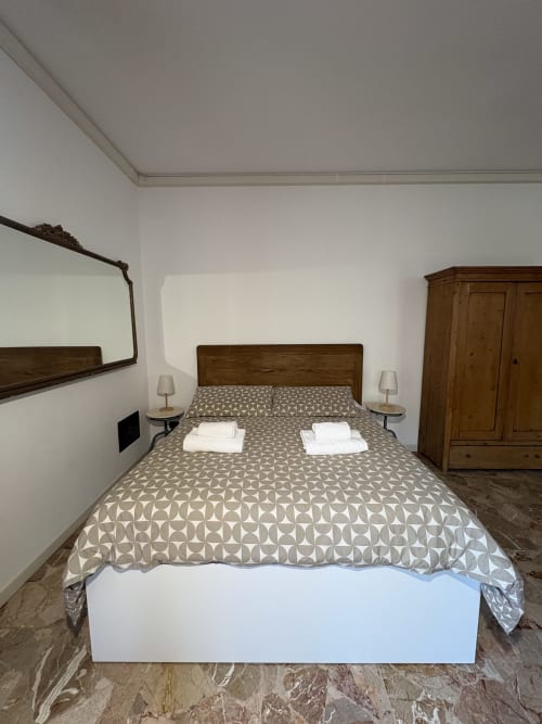 Camera da letto dell'appartamento Le Arche a Verona con letto in legno, biancheria a fantasia, lampade comodino e armadio