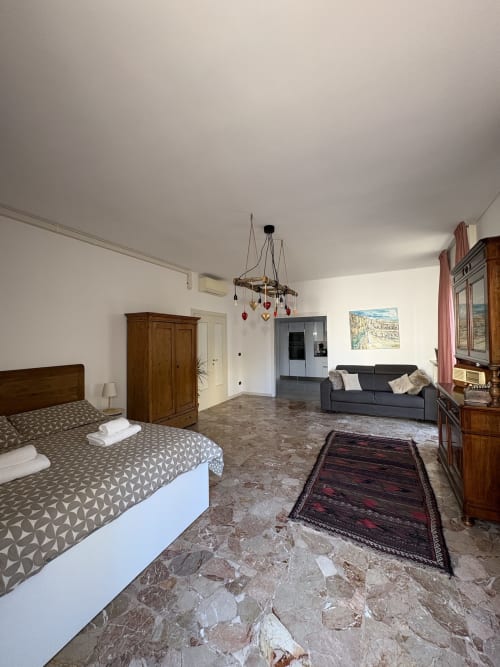 Ampio monolocale a Verona con letto in legno, divano scuro, pavimenti in marmo e comfort moderni