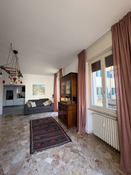 Soggiorno moderno a Verona con pavimenti in marmo, tende malva, divano scuro, mobili in legno e ampie finestre