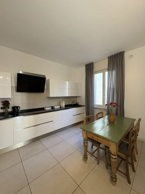 Cucina moderna con mobili bianchi, piani neri, tavolo da pranzo e accesso alla terrazza nell'appartamento di Verona
