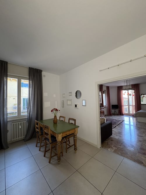 Luminosa zona pranzo dell'appartamento Le Arche a Verona con tavolo verde, sedie in legno e accesso al soggiorno