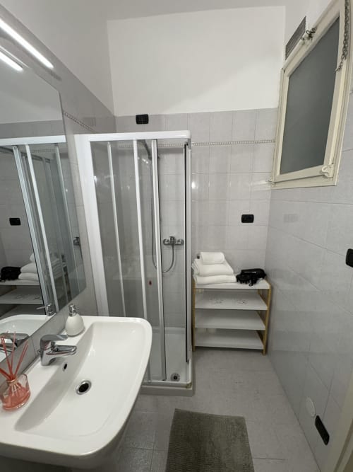 Bagno moderno dell'hotel Le Arche a Verona con lavabo bianco, box doccia in vetro e scaffali con asciugamani