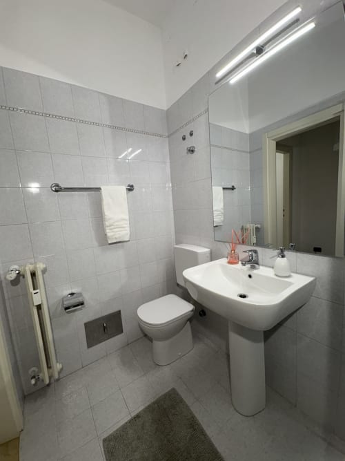 Bagno moderno dell'appartamento Le Arche a Verona con lavabo a colonna bianco, WC e zona doccia piastrellata