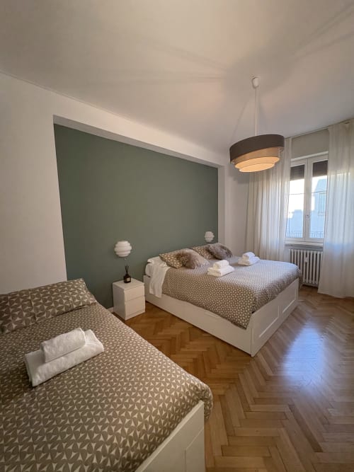 Camera moderna all'hotel Le Arche di Verona con letti gemelli, parete verde, lampada a sospensione e pavimento in parquet