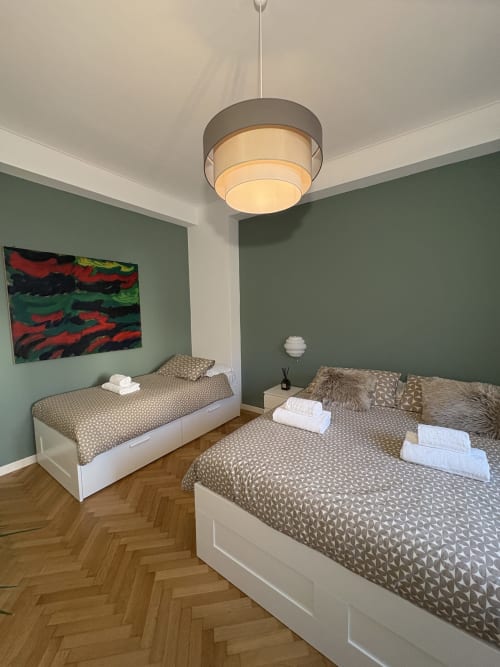 Camera moderna con due letti, pareti verde salvia, lampada a sospensione e biancheria a motivi presso l'hotel Le Arche a Verona