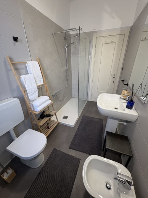 Bagno moderno dell'hotel Le Arche a Verona con doccia, lavabo, wc e portasciugamani in legno