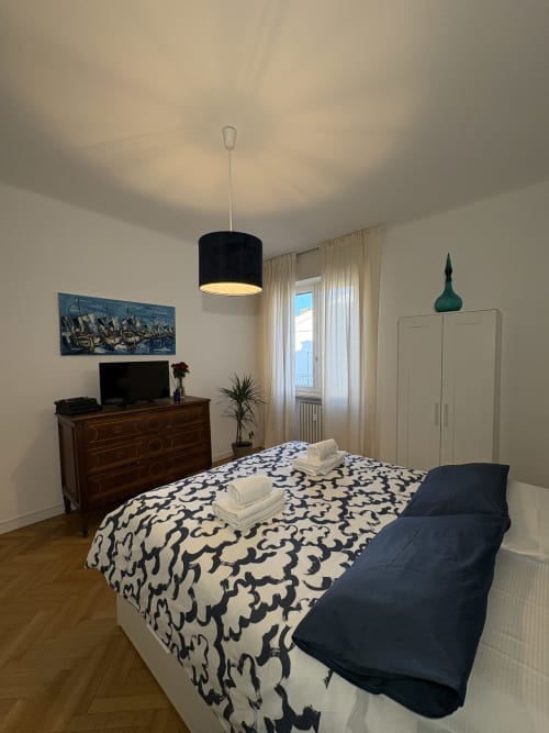 Camera moderna dell'hotel Le Arche a Verona con biancheria decorata, cassettone in legno e lampada a sospensione nera