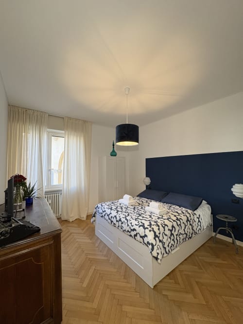 Camera moderna all'hotel Le Arche di Verona con testata navy, letto bianco, biancheria decorativa e lampade a sospensione