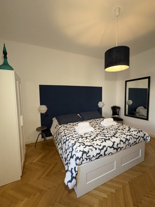 Camera moderna all'hotel Le Arche di Verona con letto bianco, testata blu scuro, biancheria patterned e illuminazione a sospensione