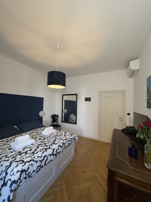 Camera moderna dell'hotel Le Arche a Verona con testata blu scuro, biancheria decorativa, lampada a sospensione e pavimento in legno