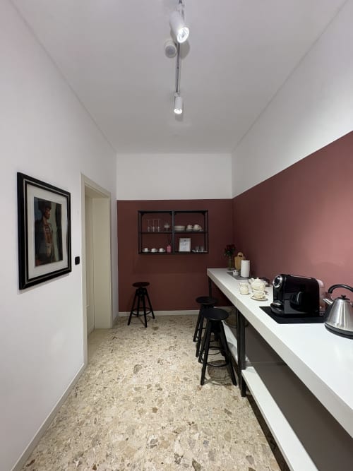 Kitchenette moderna nella camera Romeo Catullo 12 de Le Arche, Verona, con parete accent bordeaux, bancone bianco e sedute a bar.