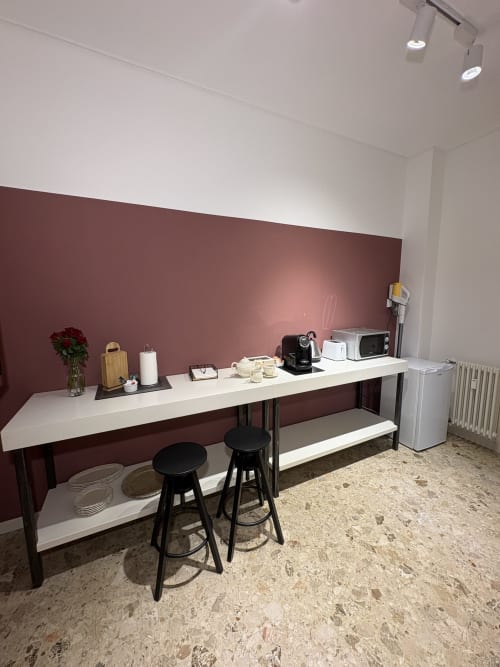 Angolo cottura moderno con parete a contrasto bordeaux, piano di lavoro bianco, sgabelli neri, elettrodomestici e pavimento in sughero a Le Arche