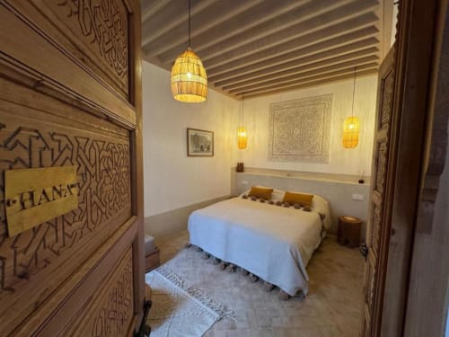 Chambre Hana Suite au Riad Casa Angelo à Marrakech avec portes sculptées traditionnelles, luminaires suspendus et lit blanc avec vue