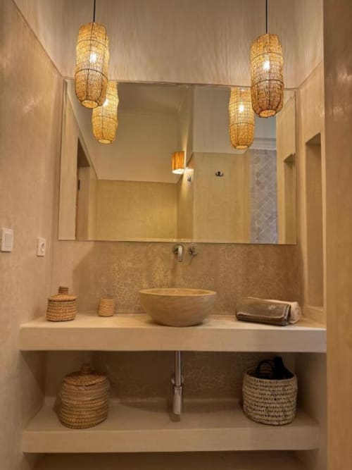 Salle de bains moderne du Riad Casa Angelo Marrakech avec vasque suspendue, luminaires en jonc tressé et rangements ouverts