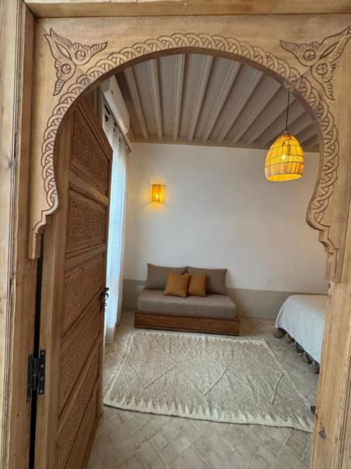 Suite Hana au Riad Casa Angelo à Marrakech avec arcades ornementales sculptées, canapé aux coussins et luminaires jaunes suspendus