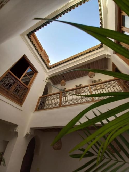 Vue de la cour de la suite Hana du Riad Casa Angelo avec balcon en bois traditionnel, puits de lumière et plantes de palmier, Marrakech