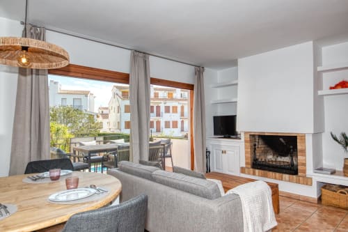 Salón lluminós de l'apartament de Palafrugell amb xemeneia, menjador i vista de la terrassa cap als edificis mediterranis