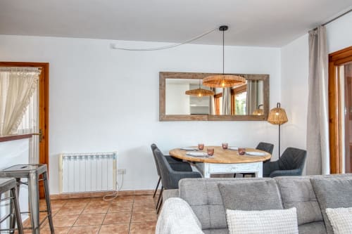 Zona de menjador moderna a l'apartament Ancora, Palafrugell, amb taula de fusta, cadires grises i llums de suspensió